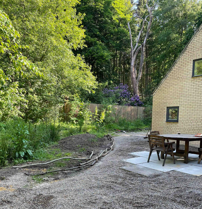 A simple outdoor seating area nestled within the woodland edge, where permeable gravel surfaces and natural materials connect the garden seamlessly with its surroundings. Outdoor seating area beside a woodland garden in the Lab Garden, Ascot, featuring permeable gravel surfacing and natural log edging — blending sustainable design with nature-based living.